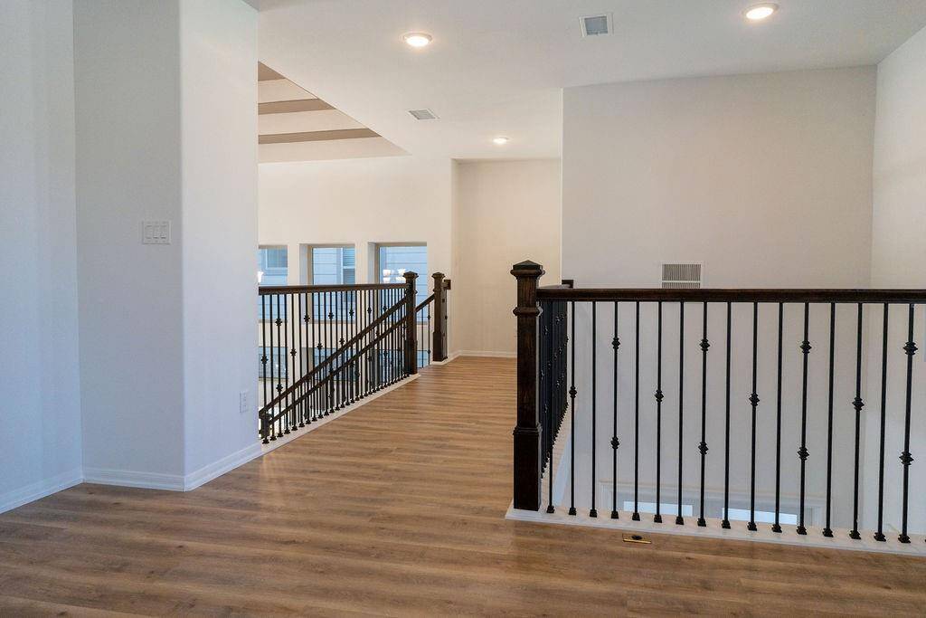 Bright, open landing area with elegant wooden flooring and a stylish wrought iron railing. The space is well-lit with recessed lighting, providing a modern and inviting atmosphere.