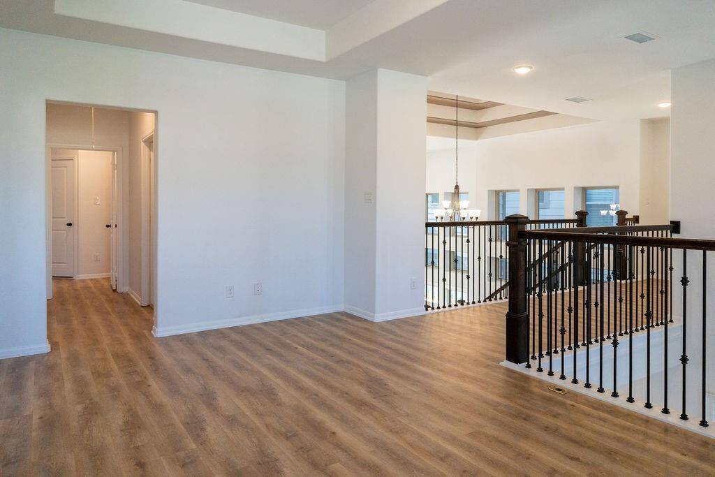 Open, airy landing area with wood flooring and elegant iron railings overlooking a lower level. The space is bright, with multiple windows and recessed lighting, offering a modern feel.