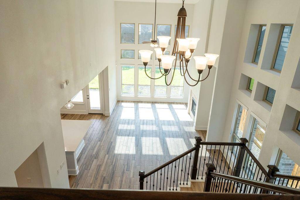 Bright and spacious open-concept living area with high ceilings and large windows. Features a stylish chandelier, wood flooring, and a modern staircase. Ideal for natural light and an airy atmosphere.