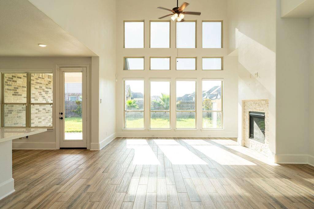 This spacious living area features high ceilings, abundant natural light from large windows, a cozy fireplace, and elegant wood flooring. It offers a seamless connection to the outdoors with a convenient door to the backyard.