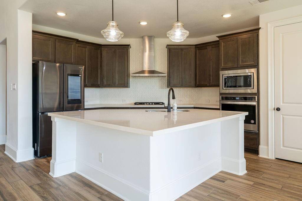 Modern kitchen with dark wood cabinets, stainless steel appliances, and a large white island. It features pendant lighting, hardwood floors, and ample counter space, ideal for cooking and entertaining.