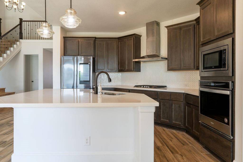 This modern kitchen features dark wood cabinetry, stainless steel appliances, and a sleek island with a sink. The open layout is enhanced by pendant lighting and a nearby staircase, creating an inviting space for cooking and entertaining.