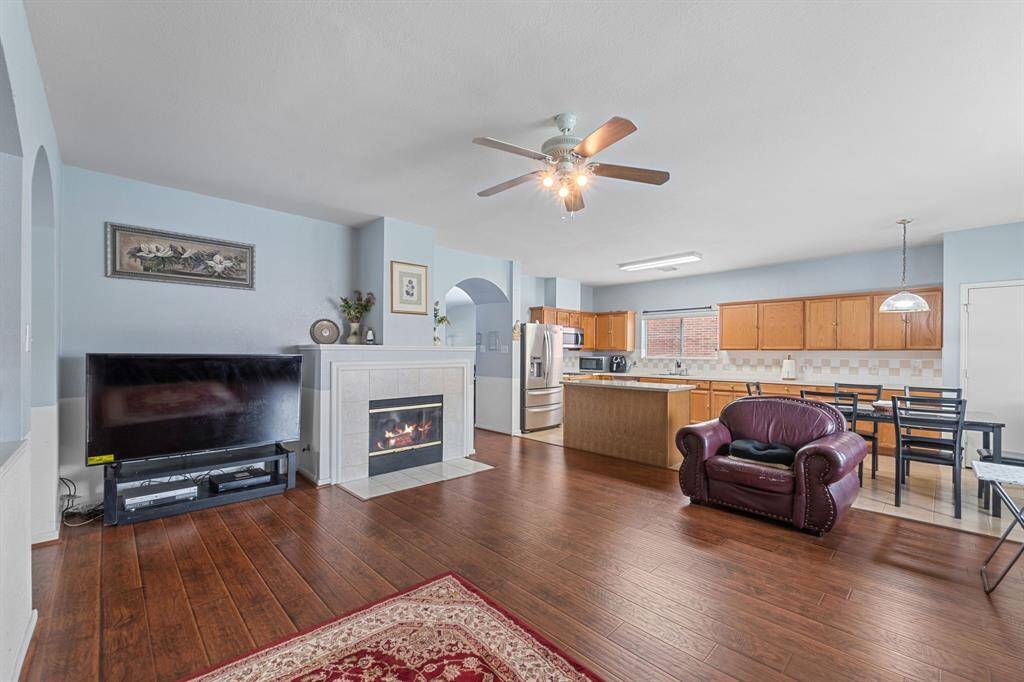 Spacious open-concept living area with hardwood floors, featuring a cozy fireplace and a ceiling fan.