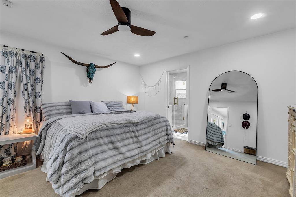 Spacious and tranquil primary bedroom with soft carpeting, stylish ceiling fan, and access to a private spa-like ensuite bathroom. Peaceful backyard views complete the retreat.