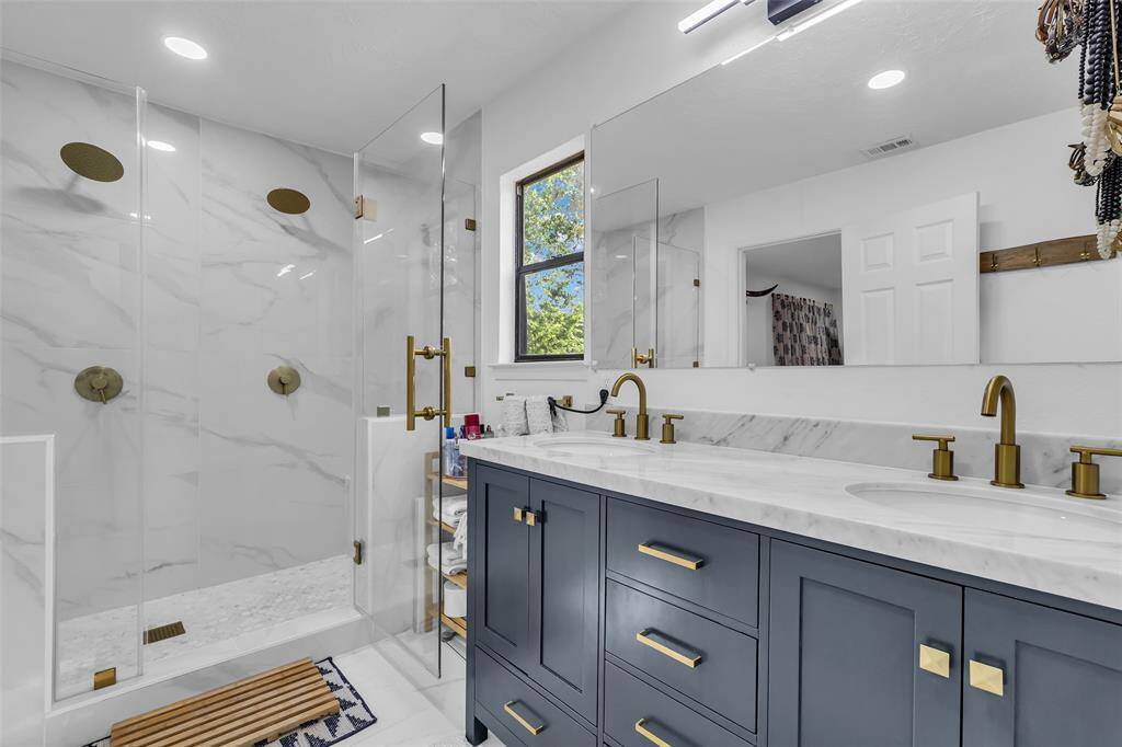 Luxuriously renovated ensuite featuring a dual-head walk-in shower, marble-look tile, double vanity with quartz counters, and matte gold fixtures for an elevated, modern touch.