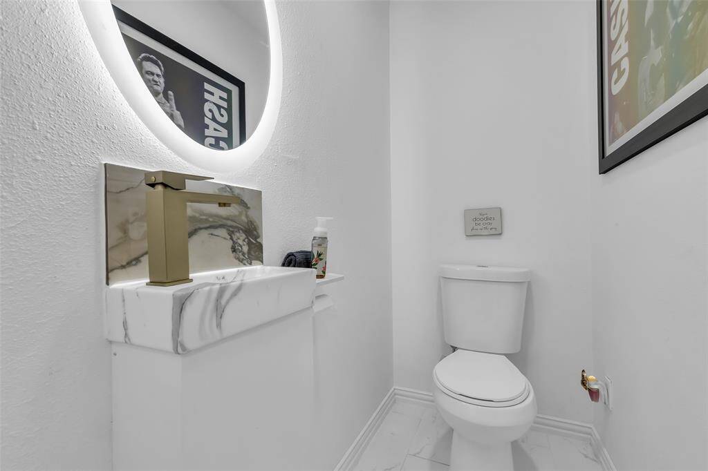 Sleek and modern half bath with custom marble vanity, backlit mirror, and stylish gold-tone fixtures. A chic space for guests.