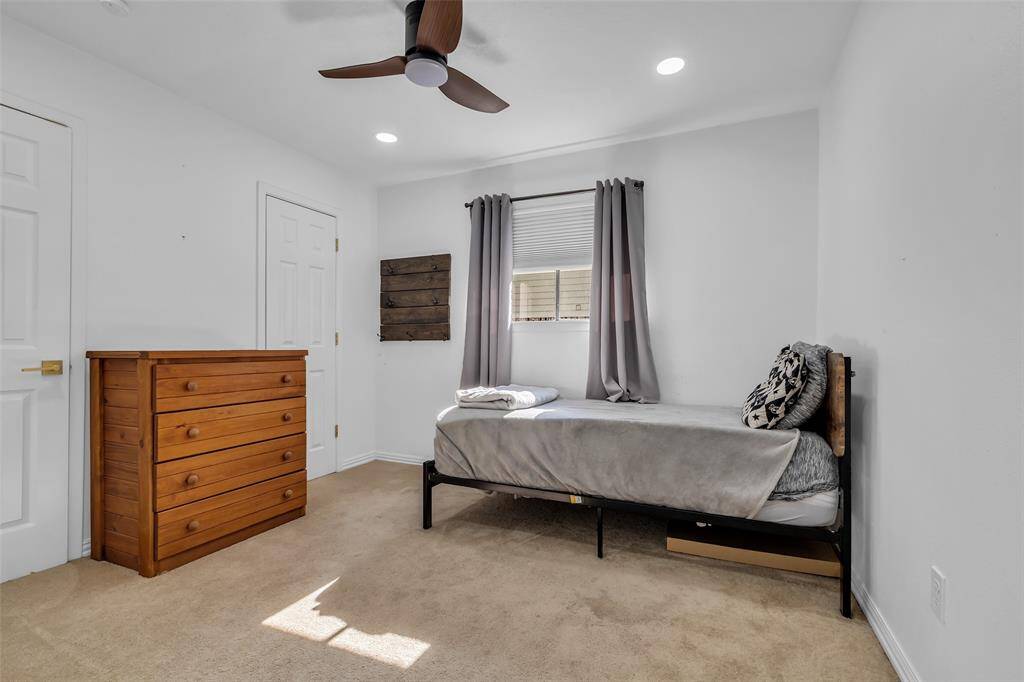 Bright bedroom with plush carpeting, neutral tones, and a large window bringing in natural light. Includes double-door closet and ceiling fan.