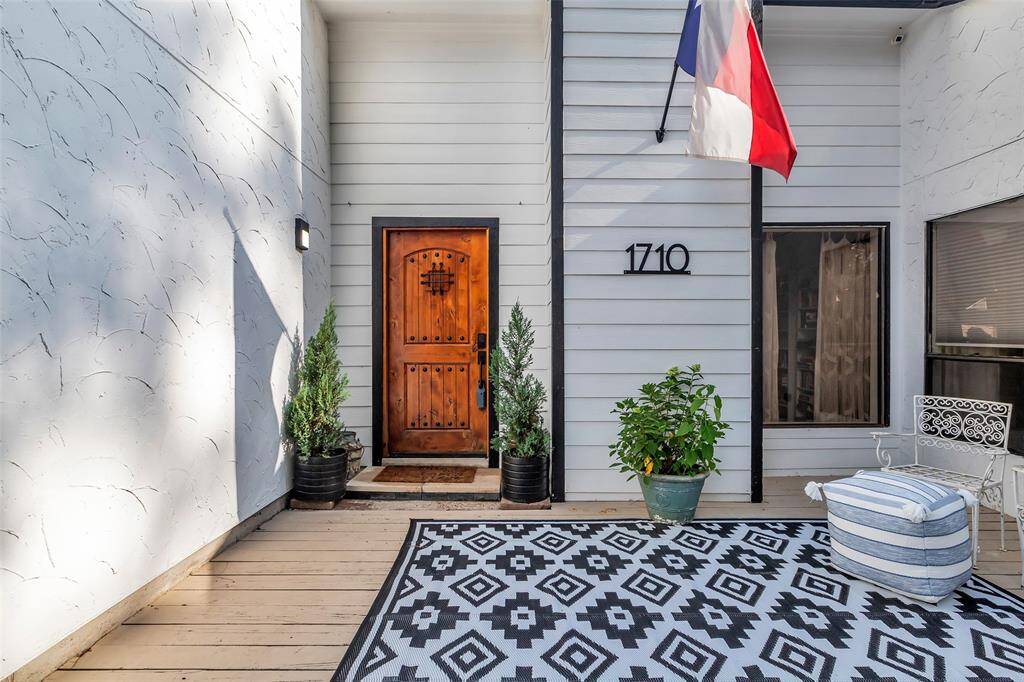 Inviting front patio with decorative rug, wrought iron furniture, and potted plants. The rich wood front door and Texas flag add warmth and personality.