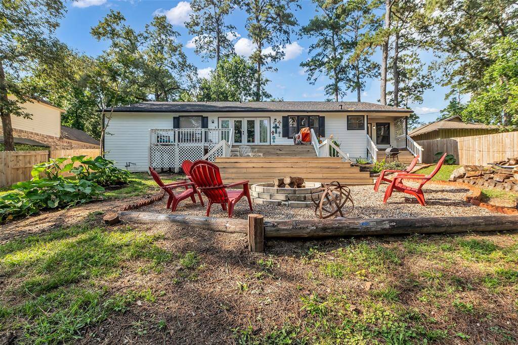 Beautiful view of the spacious, multi-level deck leading from the home to a serene backyard retreat. The fire pit area with red Adirondack chairs is perfect for cozy evenings and entertaining guests.