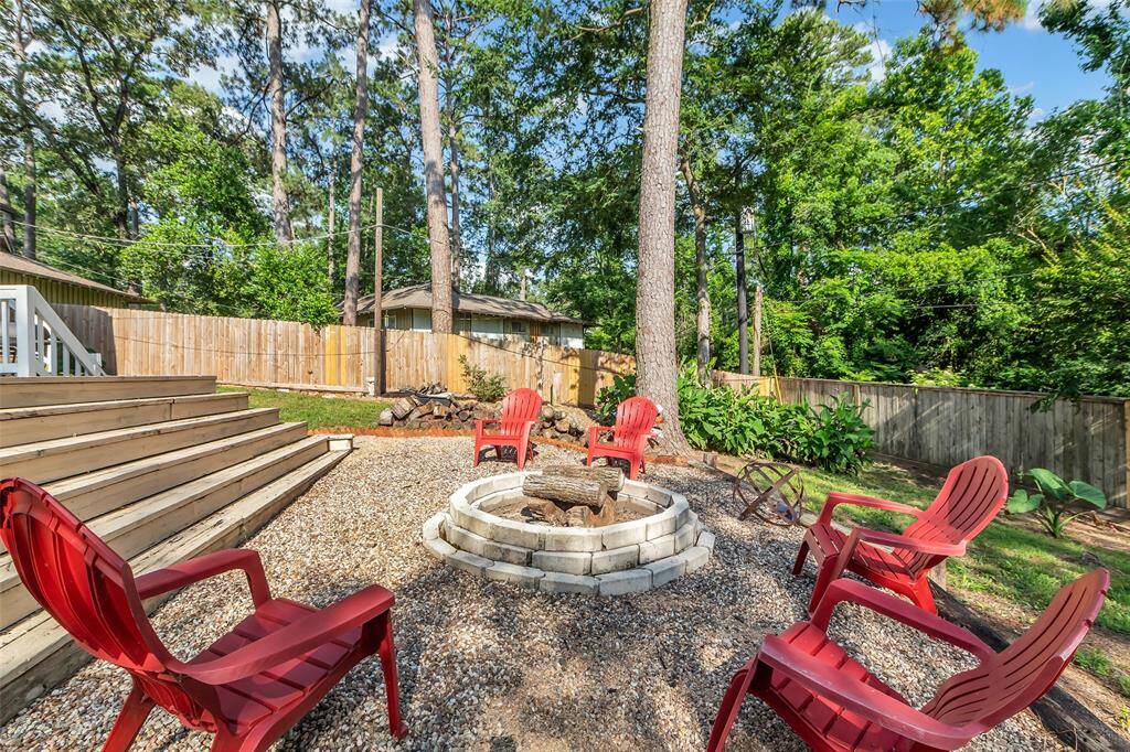 Close-up of the gravel fire pit area surrounded by tall trees and privacy fencing. A peaceful, shaded setting that feels like a woodland escape right in your backyard.