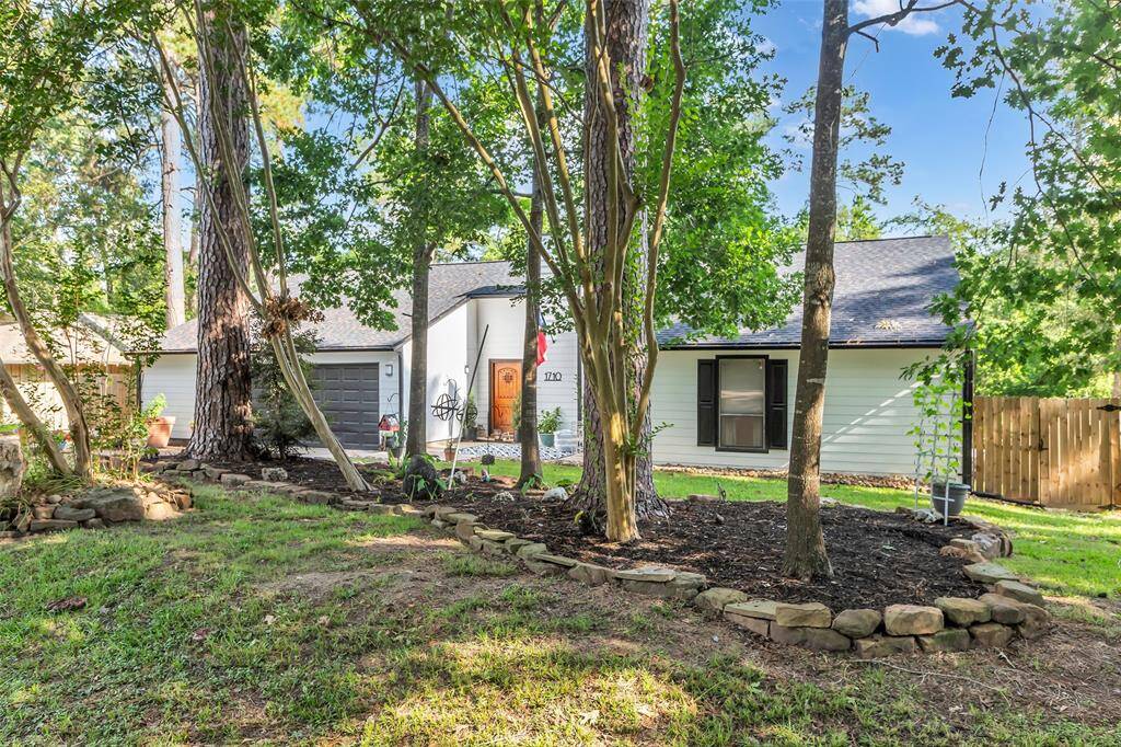 Lush, shaded front yard with mature trees, garden beds with stone edging, and a glimpse of the welcoming entryway – a perfect mix of nature and charm.