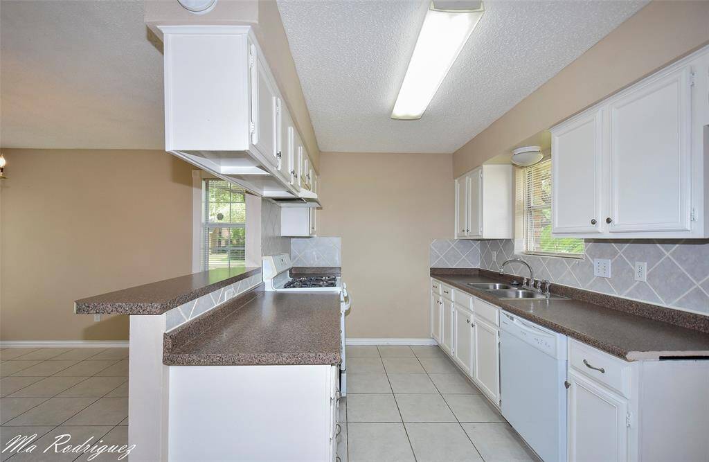 Bright kitchen with white cabinetry, and tiled backsplash. Features a gas stove, and ample natural light from the window. Open layout with a breakfast bar overlooking the dining area.