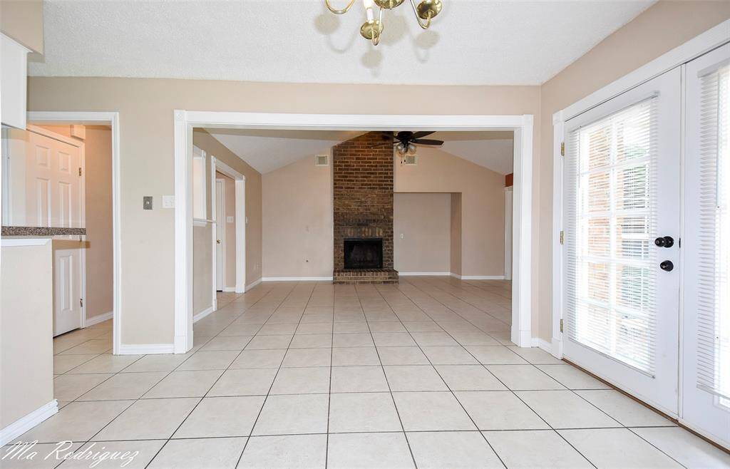 Bright living area with tile flooring, a brick fireplace, offering plenty of natural light and an open layout. Perfect for a cozy and inviting home atmosphere.