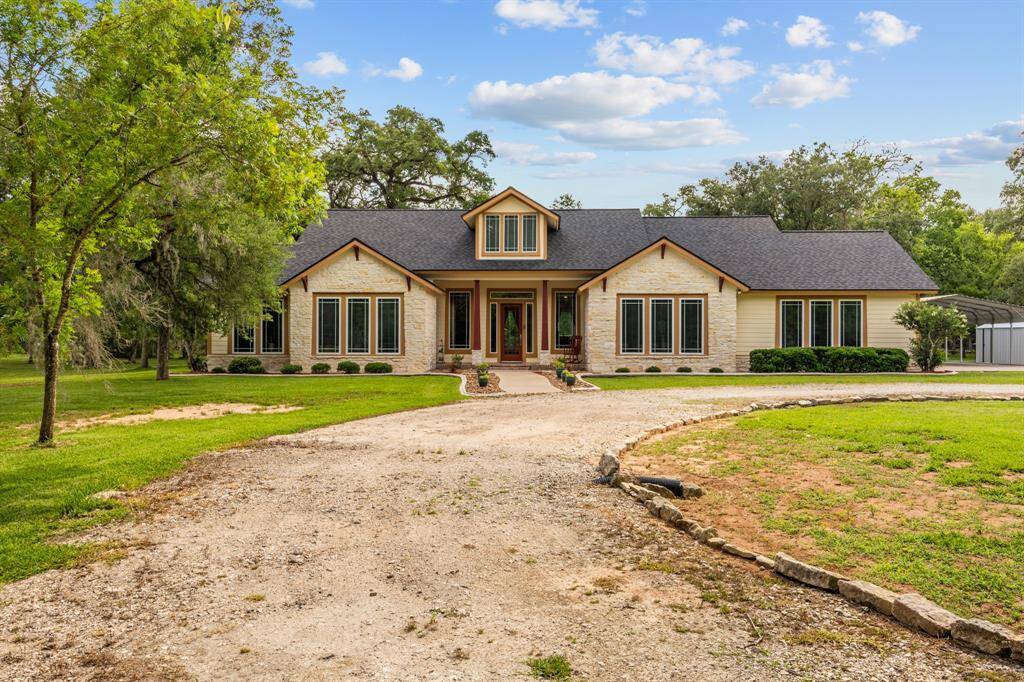Striking stone-and-siding façade with a covered porch entry and dormer detail, all set against 5.3 wooded acres—luxury country living at its finest.