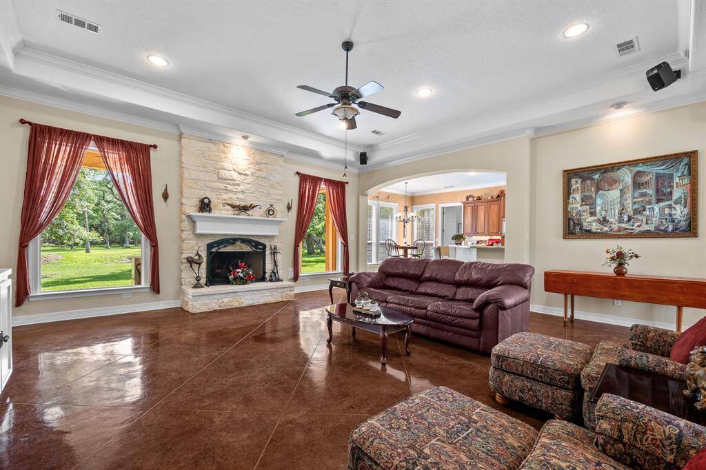 Vaulted tray ceiling, full-height limestone fireplace and recessed lighting frame this inviting gathering space—rich drapes and oversized windows flood the room with natural light and woodland views.