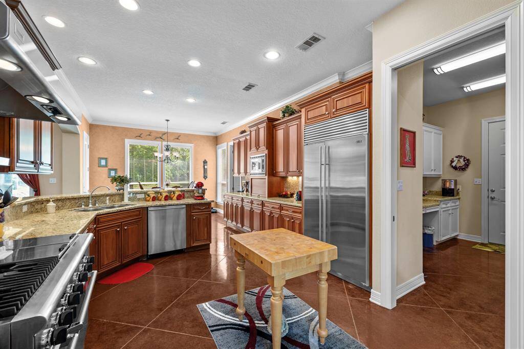 Cherry-stained cabinetry stretches wall-to-wall, flanked by granite counters, under-cabinet lighting and a built-in Sub-Zero refrigerator—pantry access just beyond. And a floor outlet under the portable island.