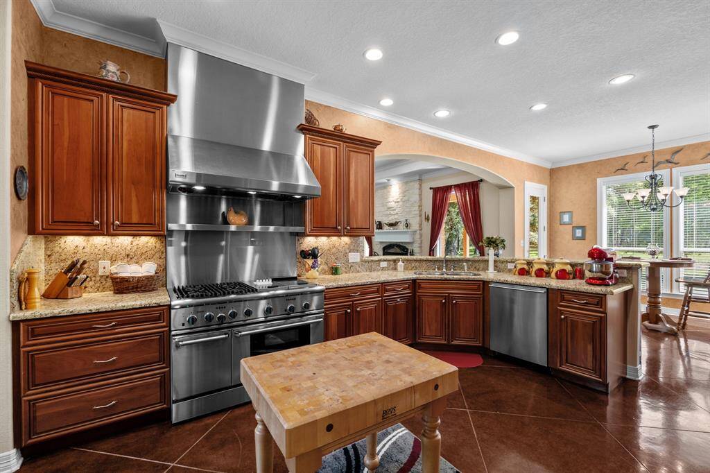 Thermador 48” six-burner range beneath a sleek stainless steel hood, set against a granite backsplash with a butcher-block prep island at center. Double-oven for ease of meal preparation for those big functions.