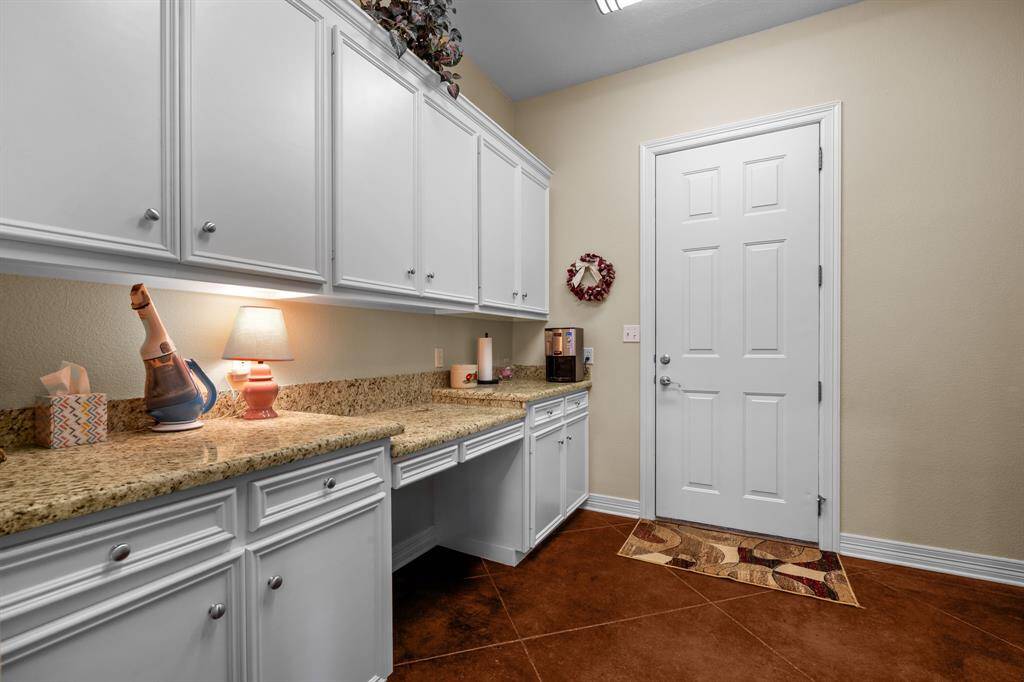White shaker cabinets, a granite landing counter, and desk nook flank the exterior door—perfect for organizing gear.