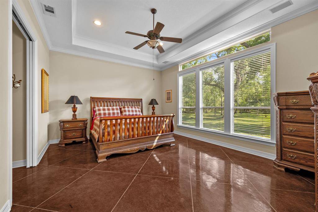 Tranquil owner’s retreat with soaring tray ceiling, ceiling fan, and a wall of picture windows plus high transom light—flooded with natural light and overlooking the lush backyard.