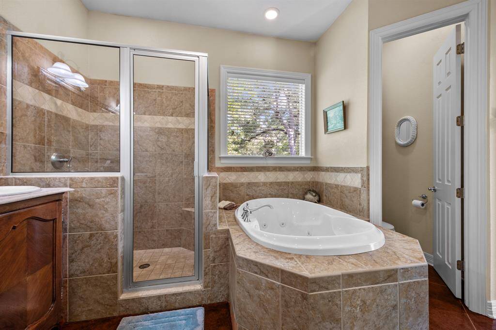 Corner-mounted jetted soaking tub beside a walk-in shower, all wrapped in premium tile for a true spa experience.