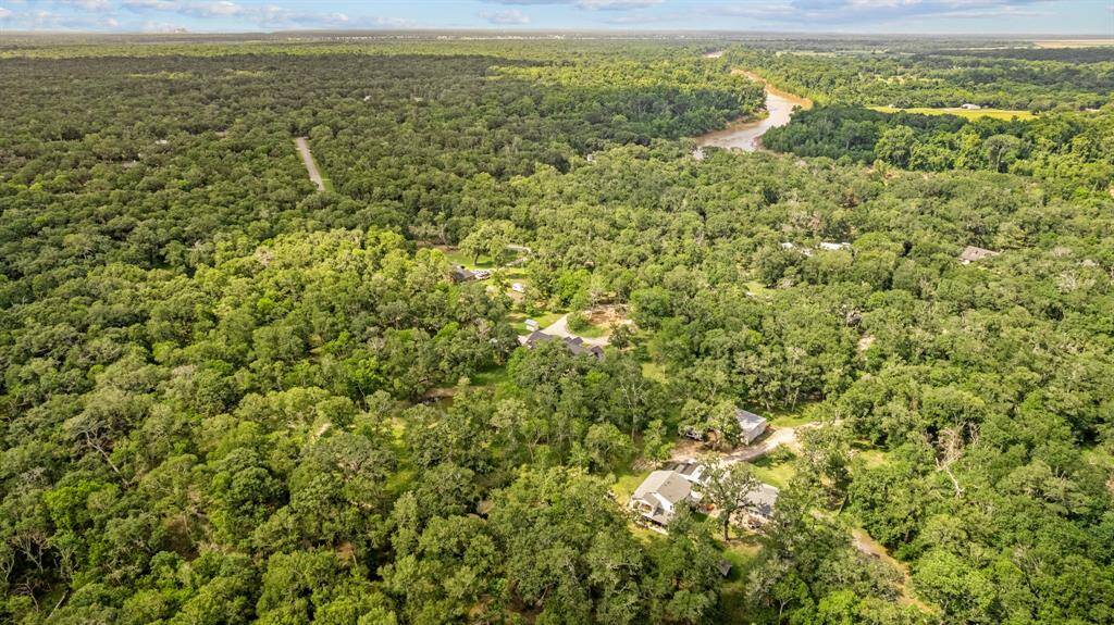High-elevation view looking across the property, illustrating dense canopy coverage, the curving drive and nearby Brazos River corridor.