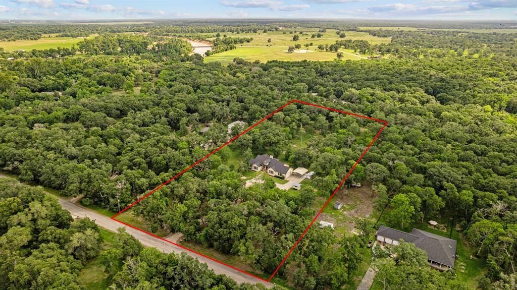 Drone shot revealing the home nestled amid live oaks on a heavily treed 5.3 acre parcel with the lot boundaries.