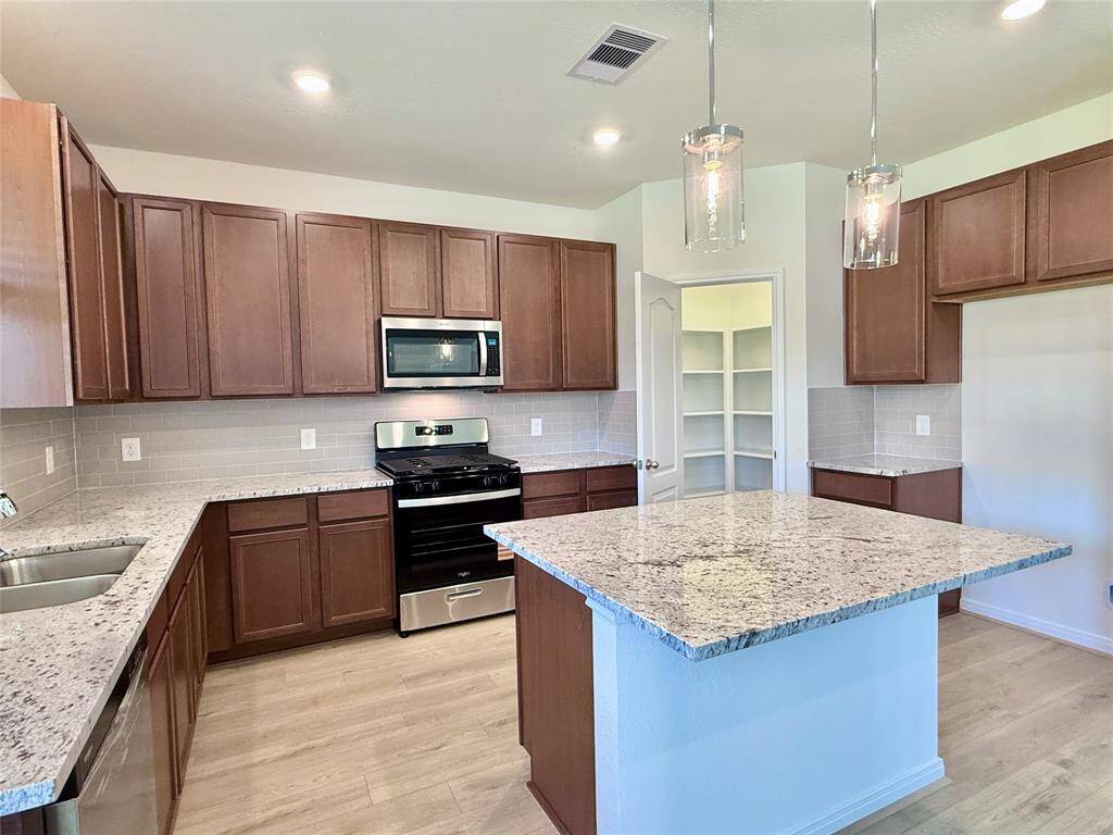 From here, enjoy views of the granite countertop, extended island with breakfast bar, stainless steel appliances, and 42” cabinets.