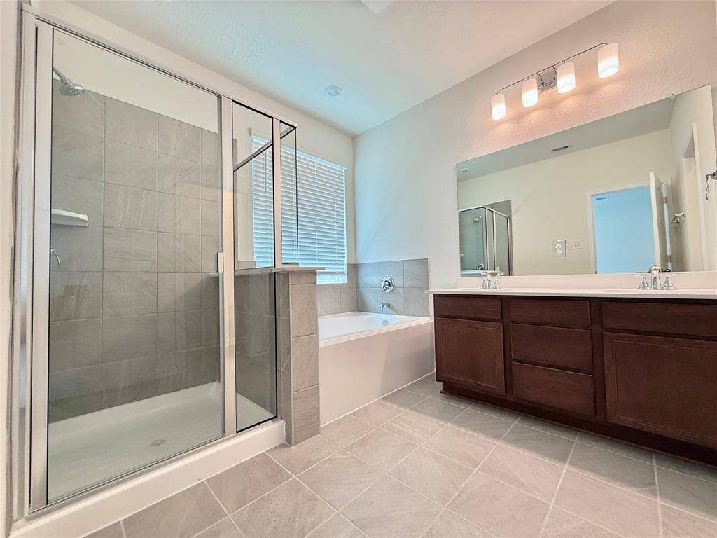 Upgraded primary bathroom features a large soaking tub, glass-enclosed shower, dual vanity sinks, and stylish light fixtures.