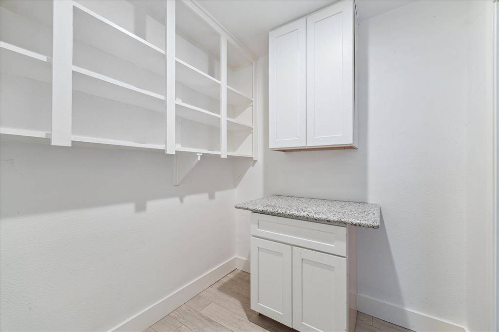Large air conditioned, remodeled laundry room with a wall of shelving and a granite covered folding station.