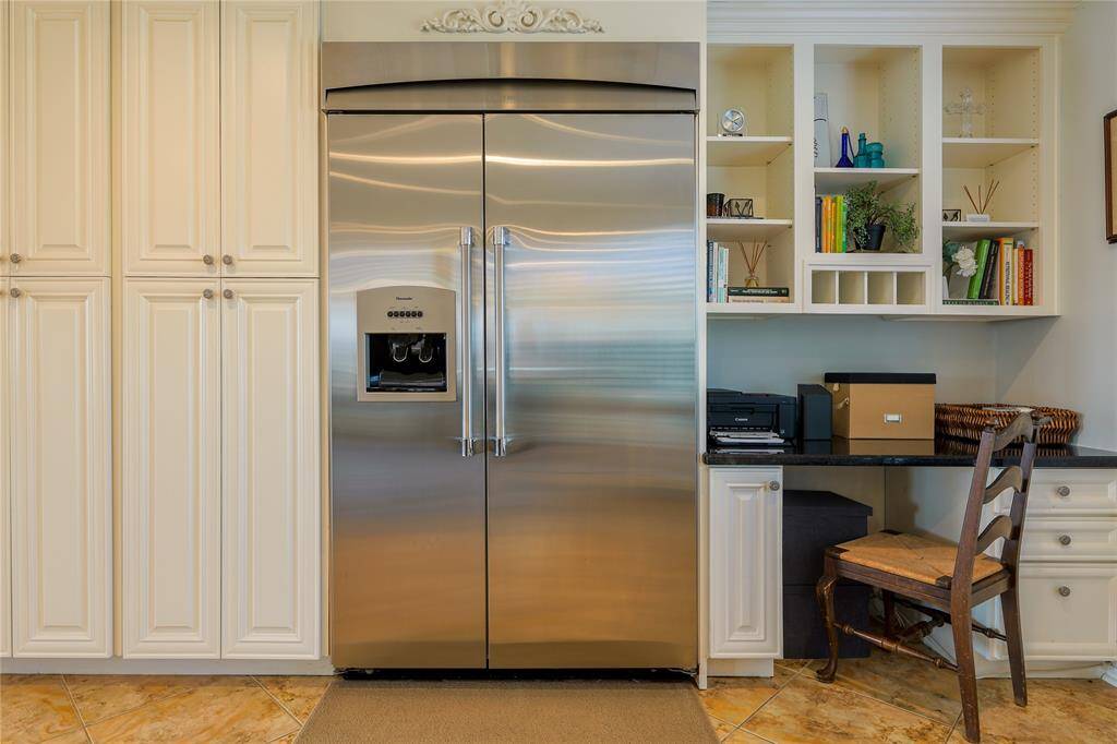 This kitchen features a high-end Thermador refrigerator, surrounded by ample cabinetry for storage. A built-in desk area with shelving provides a functional workspace!