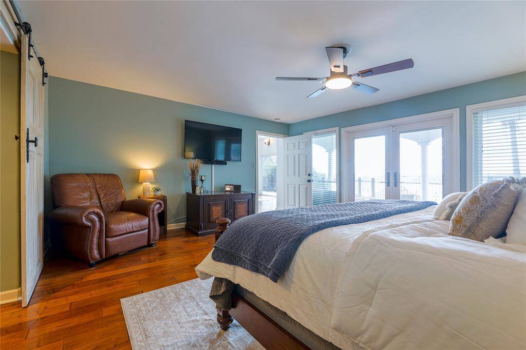 The primary bedroom also boasts large windows and glass doors leading to an outdoor area, filling the room with natural light. The soft blue walls and ceiling fan add a calming touch.