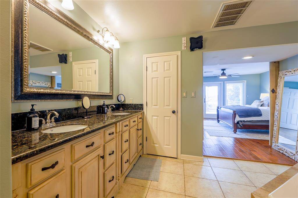 This photo showcases the spacious primary bathroom with a dual-sink vanity, featuring granite countertops and ample storage.