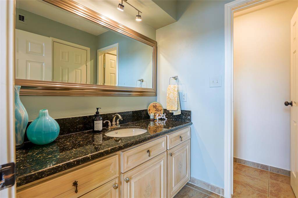 This bathroom features a spacious vanity with a dark granite countertop, elegant fixtures, and ample cabinet storage. A large mirror enhances the space, while soft lighting adds warmth.