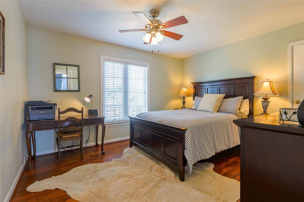 This cozy guest bedroom features warm hardwood floors, a ceiling fan, and plenty of natural lighting.