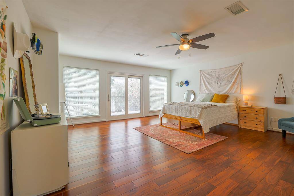 This spacious bedroom features hardwood floors, large windows letting in ample natural light, a ceiling fan, and a cozy bed setup. Just through the sliding glass doors, enjoy a perfect morning/evening on the balcony!