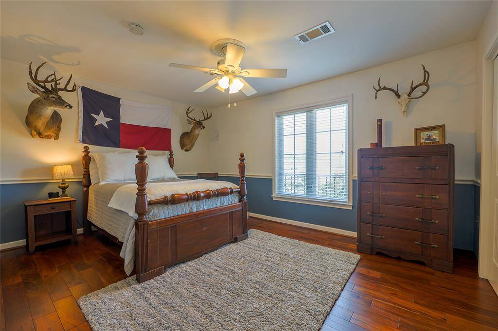 This cozy bedroom features wooden flooring, a ceiling fan, and a large window for natural light.