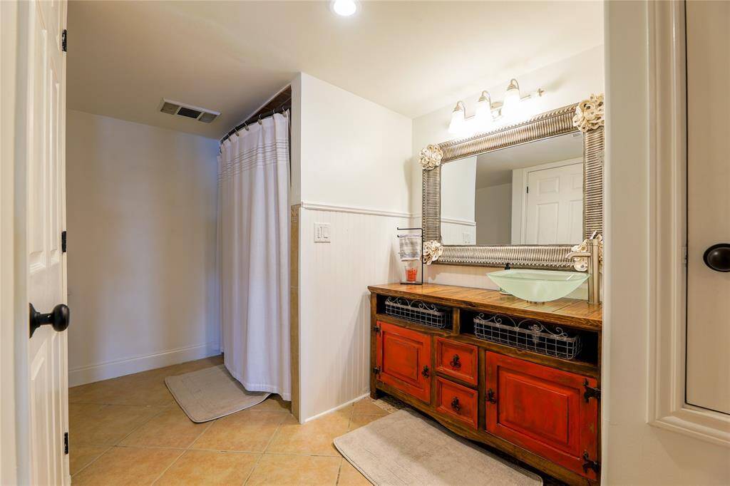 This bathroom features a spacious shower and a distinctive vanity with a large decorative mirror. The vanity has a rustic red finish, glass bowl sink, and ample storage, creating a warm, inviting atmosphere.
