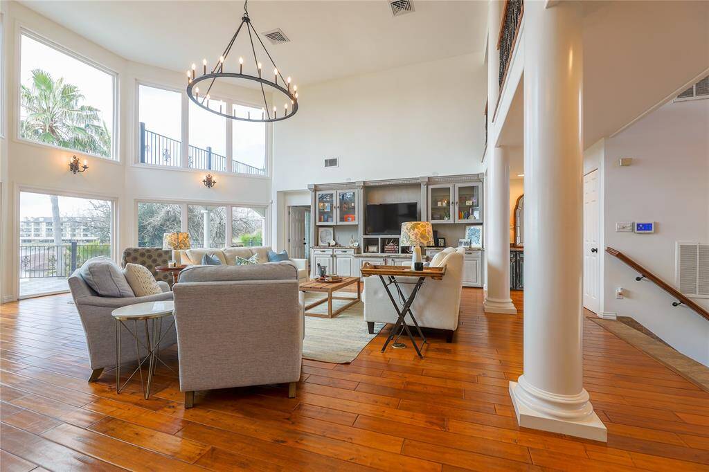 This spacious living area features high ceilings, large windows, and hardwood floors. It includes a stylish chandelier, cozy seating area, and built-in shelving. The open layout and natural light create an inviting atmosphere, with a view of the stunning outdoor space.