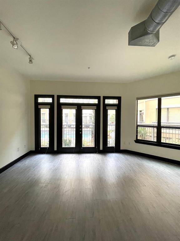 This room features a modern, open layout with large windows and glass doors, allowing plenty of natural light. It has sleek flooring, recessed lighting, and an industrial-style ceiling vent, creating a contemporary feel. Ideal for a bright, airy living space.