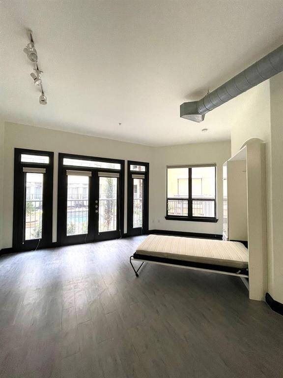 The room features modern track lighting, an exposed duct, and a pull-down bed, ideal for maximizing space.