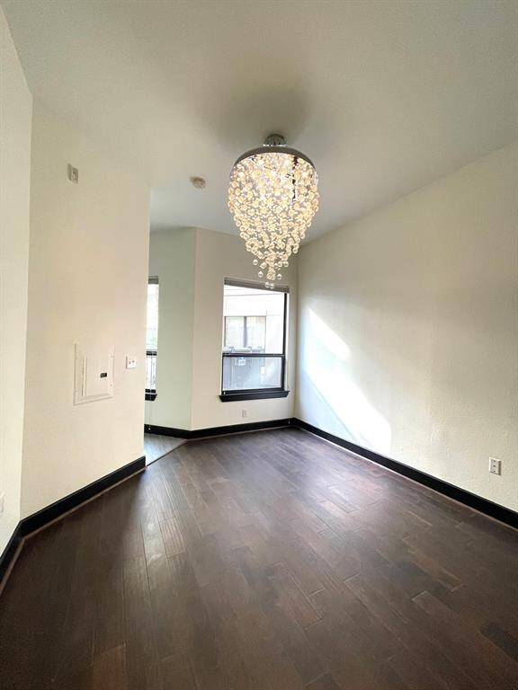The bedroom features a modern, elegant chandelier and dark hardwood floors, with ample natural light streaming through large windows.
