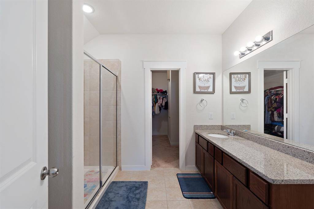 Primary bathroom featuring a spacious walk-in shower, extended countertop and warm cabinetry. Neutral finishes create a serene, spa-like atmosphere.