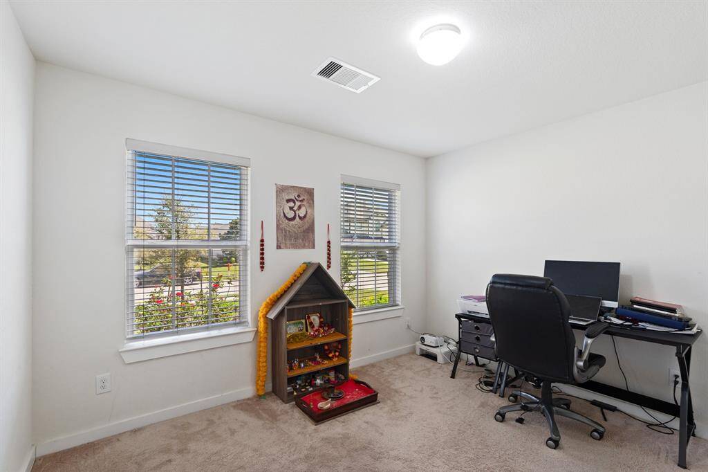 Secondary bedroom on the main floor, featuring soft carpeting and large windows that provide a lovely view of the front of the home. A perfect space for guests, a home office, or a private retreat!