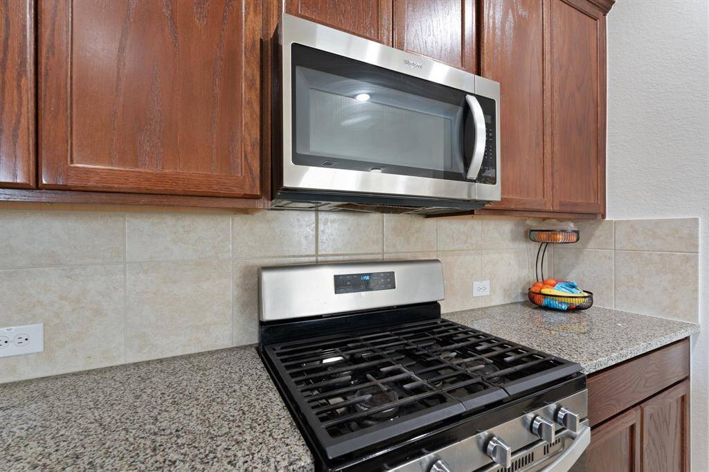 The stainless steel microwave and gas range offers the perfect setup for preparing meals with ease, while the custom backsplash adds a unique touch of elegance and charm. Whether you're cooking for a crowd or enjoying a quiet meal, this kitchen effortlessly combines beauty with practicality.