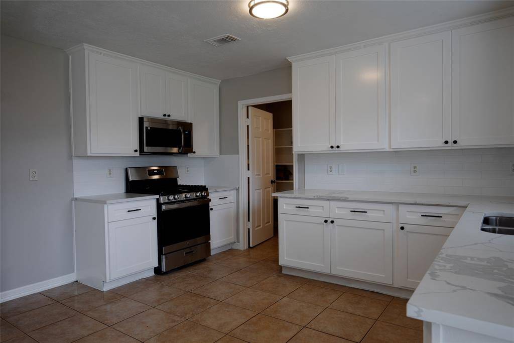 Kitchen with quartz counters, new gas range, new microwave and new dishwasher. Opens to den with view of backyard