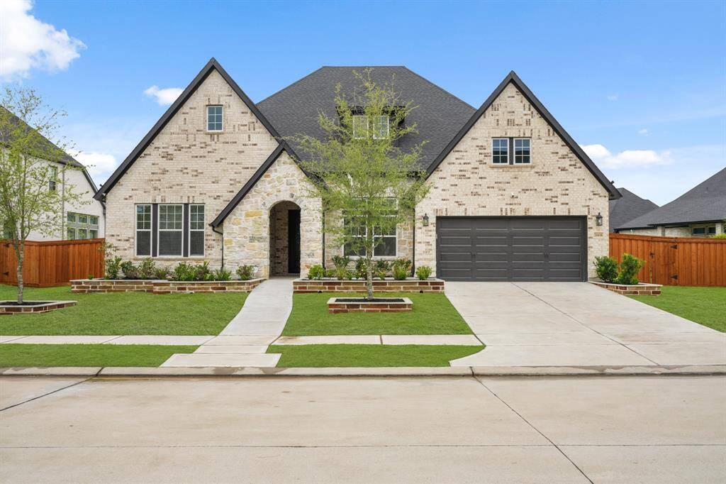This photo shows a modern, brick home with a spacious driveway leading to a double garage. The front yard is neatly landscaped with a pathway to the entrance, framed by small trees and shrubs. The house features a combination of stone and brickwork, adding to its curb appeal.