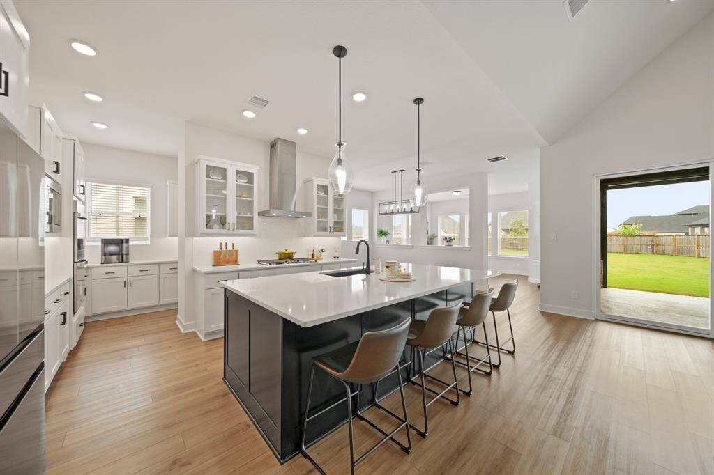 This photo showcases a modern, spacious kitchen with sleek white cabinetry, stainless steel appliances, and a large island with seating. The open layout offers plenty of natural light and views of a well-maintained backyard through large sliding glass doors. Perfect for entertaining.