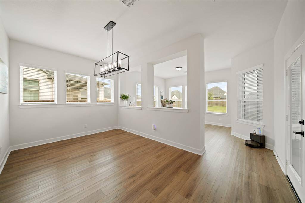 This bright, open breakfast nook features wood flooring, large windows for natural light, and a modern light fixture. Offers a view into an adjacent space, enhancing the home's flow.