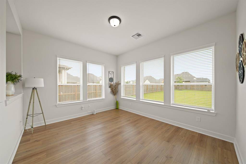 Bright and airy room with large windows offering plenty of natural light. It features light wood flooring and neutral walls, creating a versatile space overlooking a fenced backyard.