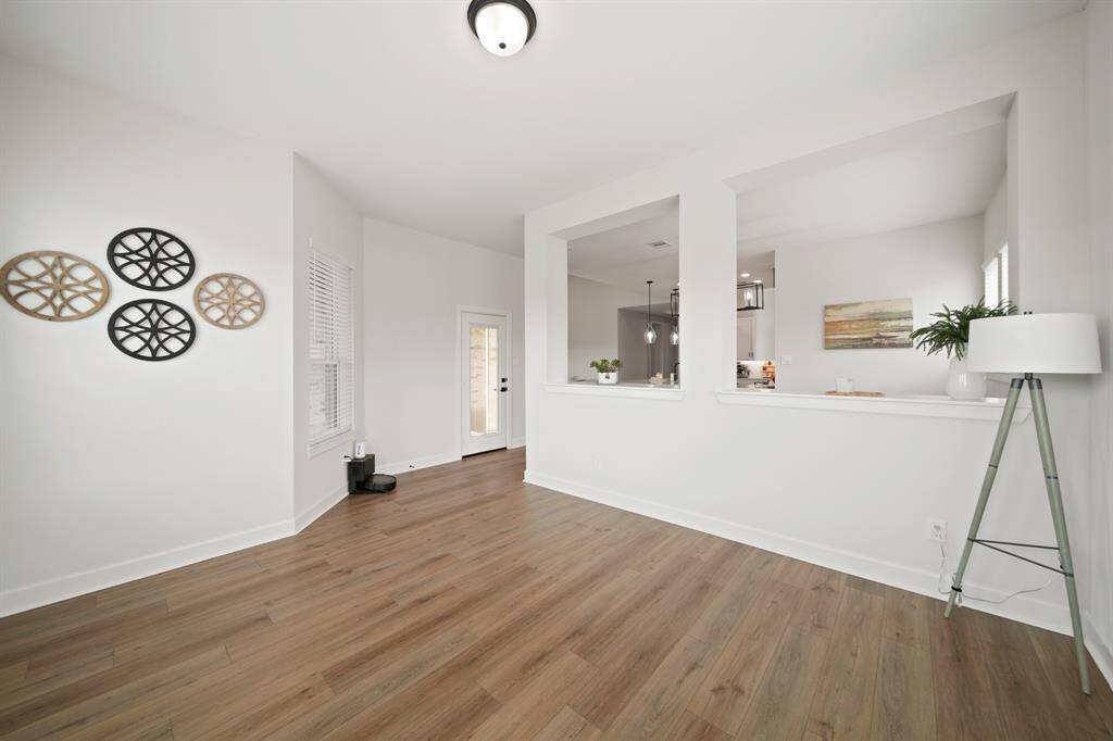 This bright, open-concept space features wood flooring, white walls, and a modern, minimalistic design. It includes a large window and a door leading outside.